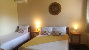 A hotel room with two single beds, a large bed, a wall-mounted air conditioner, and a decorative plate above the large bed. - Chalés Flor de Manacá (Alto Paraíso de Goiás)
