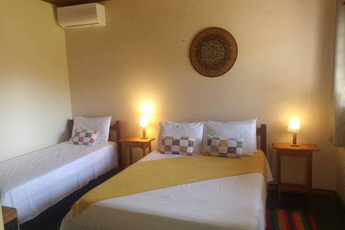 A hotel room with two single beds, a large bed, a wall-mounted air conditioner, and a decorative plate above the large bed.