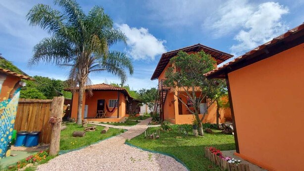 A courtyard with two houses, a palm tree, and a gravel path. - Chalés Flor de Manacá (Alto Paraíso de Goiás)