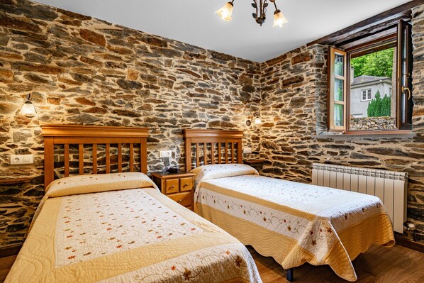 Un dormitorio con paredes de piedra, dos camas de madera, una ventana con vistas y un radiador.