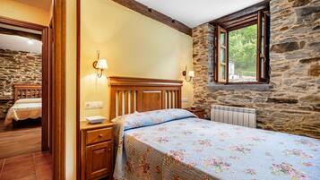 A bedroom with a wooden headboard, a floral bedspread, a stone wall, and a window with a view.