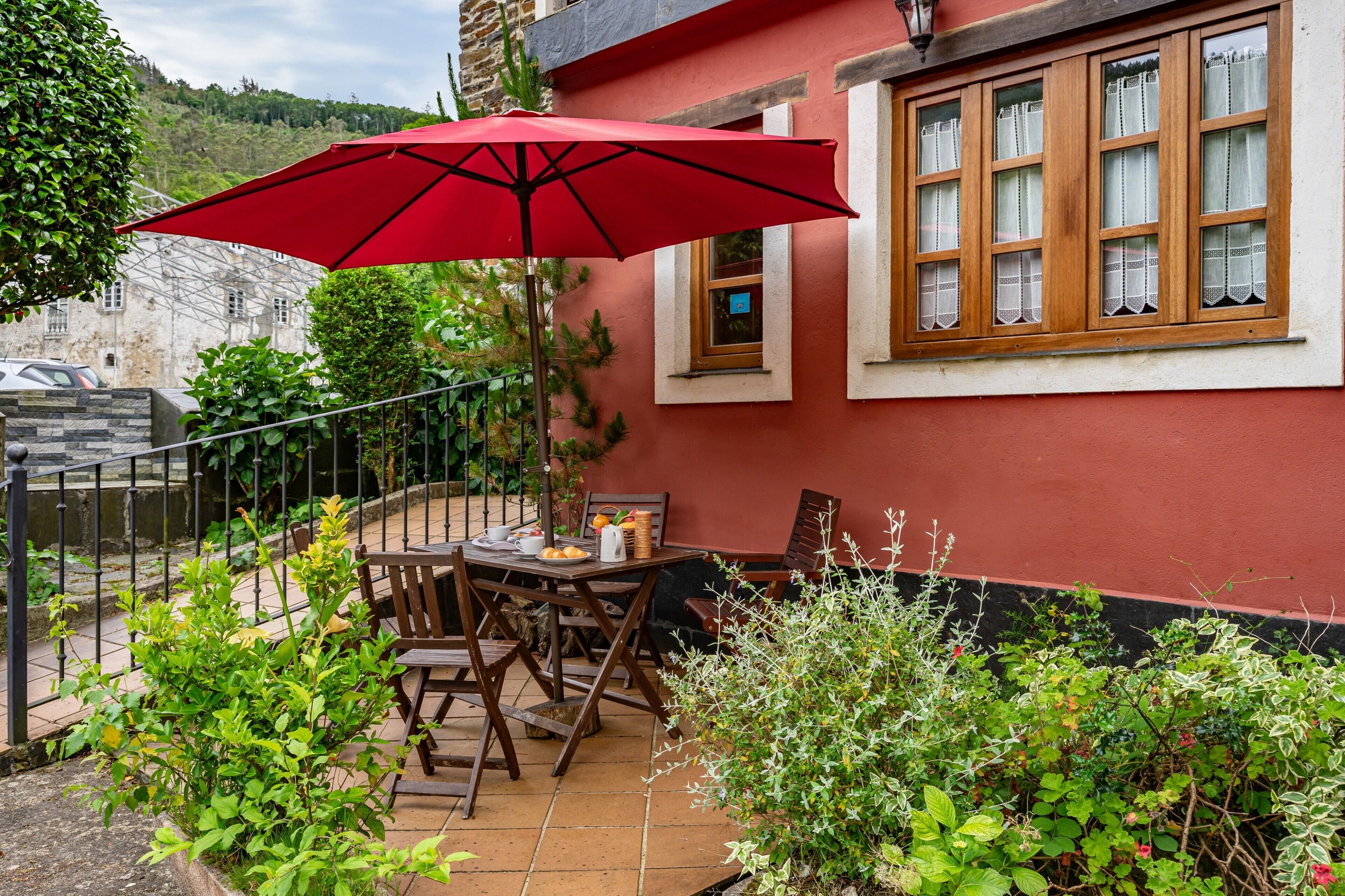 En terrasse med et bord og stole, en rød parasol og en bygning med vinduer.