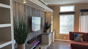 A living room with a fireplace, a large potted plant, a sofa, and a window with blinds. - Charming 2-bedroom House with WiFi, Patio/Grill, W&D, & Complimentary Breakfast (La Plata)