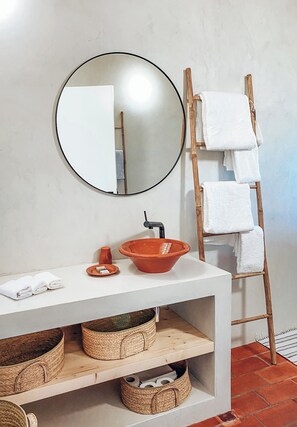 A bathroom with a white vanity, a round mirror, a wooden towel rack, and woven baskets. - Monte da Moita Nova (Odemira)