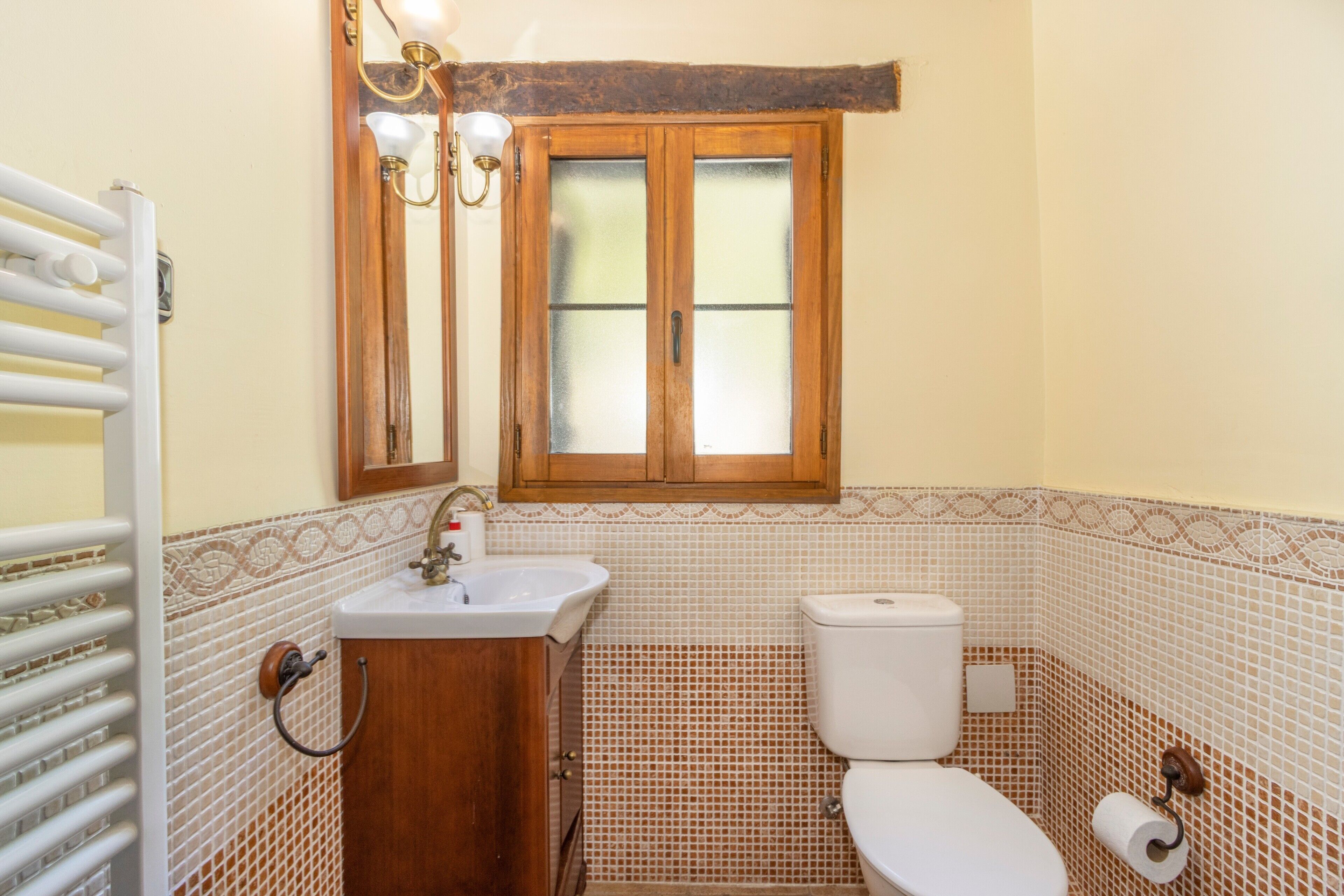 A bathroom with a wooden cabinet, a sink, a toilet, a window, and a towel rack.
