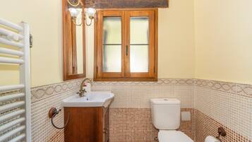 A bathroom with a wooden cabinet, a sink, a toilet, a window, and a towel rack.