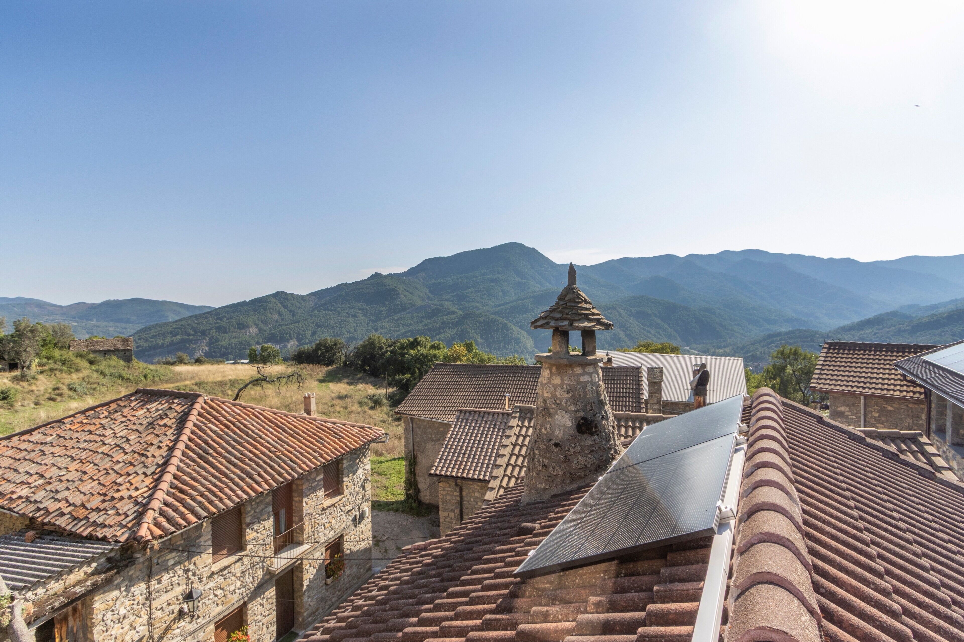 A traditional stone building with a tiled roof, a bell tower, and a view of mountains.
