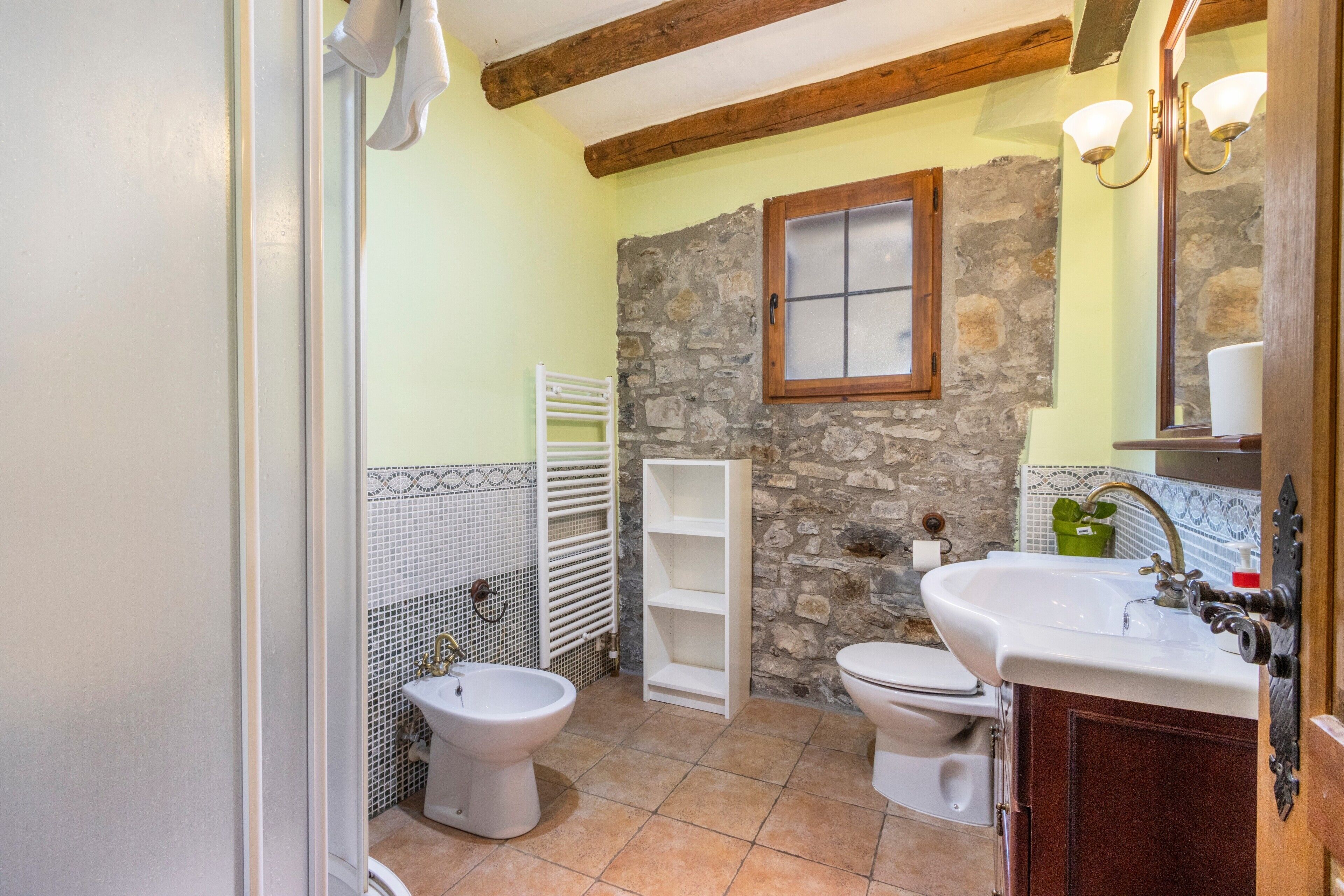 A bathroom with a stone wall, a white sink, a bidet, and a toilet.