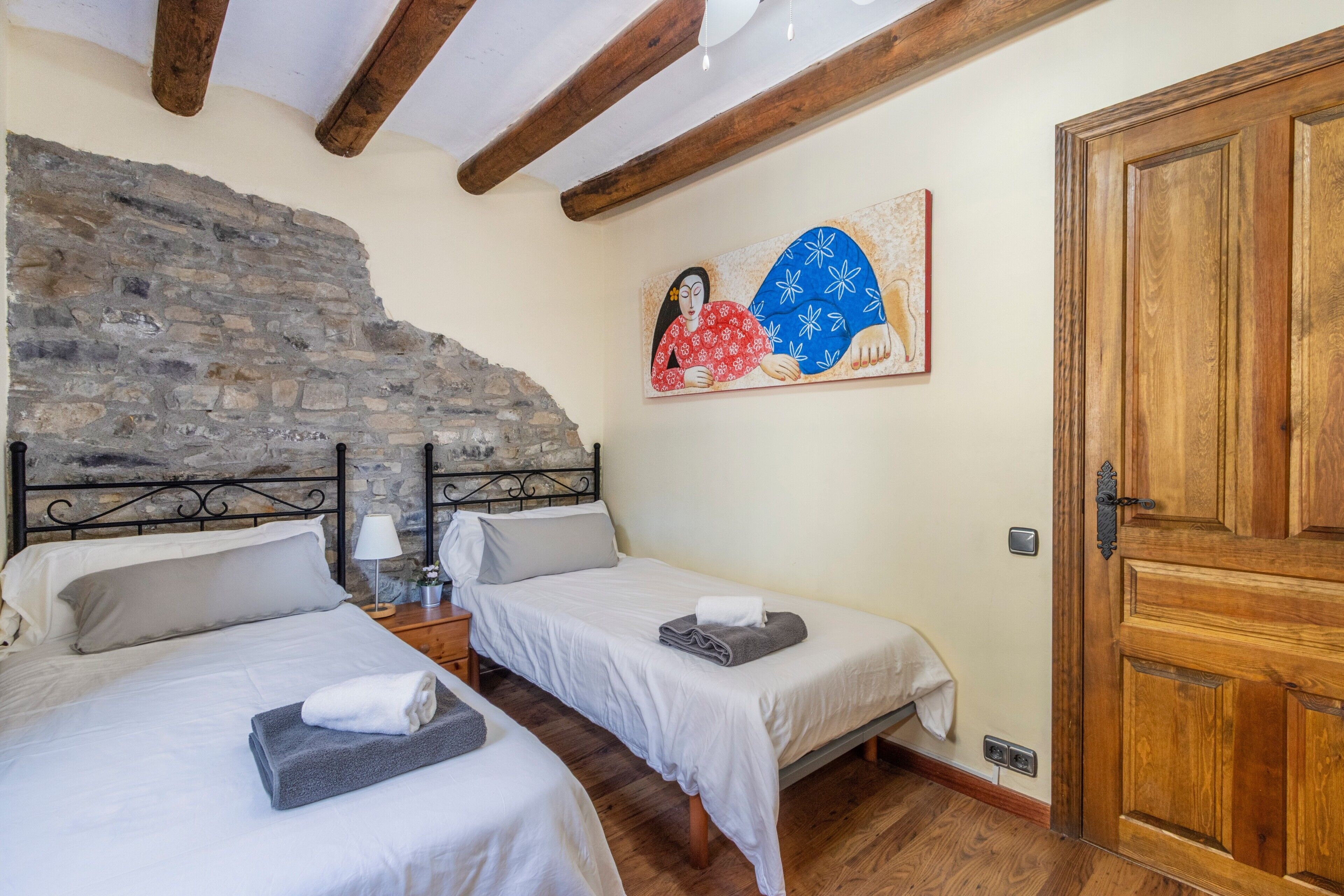 A room with two beds, a stone wall, a wooden door, and a painting on the wall.