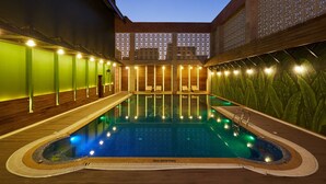A swimming pool with a 'NO DIVING' sign, surrounded by lounge areas with wooden flooring and green walls. - Club Anandam (Raipur)
