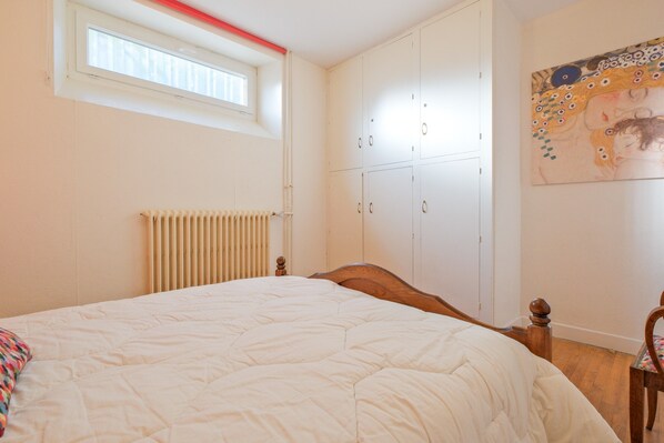 A bedroom with a bed, a radiator, a window, and a wardrobe.