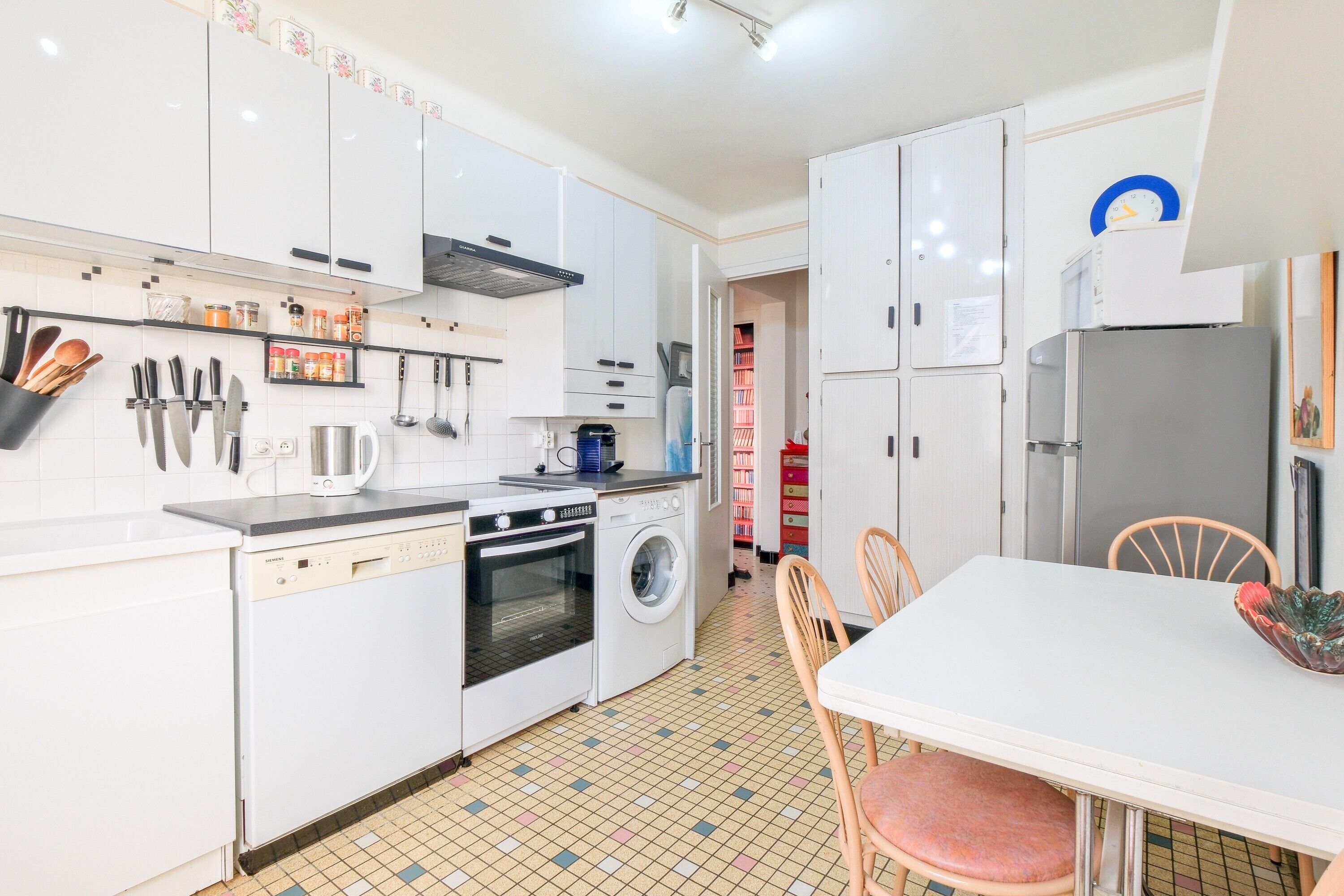 A kitchen with white cabinets, a dishwasher, an oven, a washing machine, and a dining table with chairs.