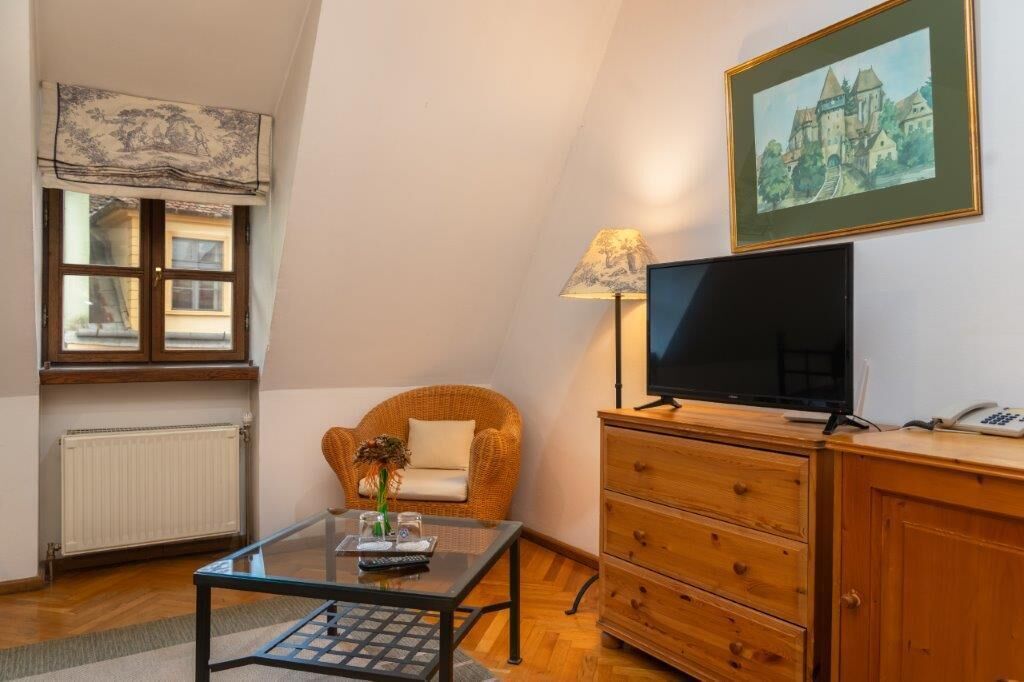 Een gezellige woonkamer met een televisie, een rieten stoel, een glazen salontafel, een houten kast en een schilderij aan de muur.