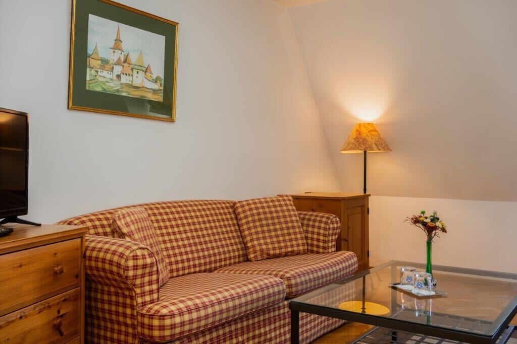 A cozy living room with a plaid sofa, a glass coffee table, a lamp, and a painting on the wall.