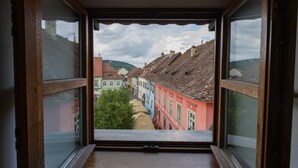 Une fenêtre étroite, d’où l’on aperçoit des bâtiments aux couleurs vives et un arbre au premier plan.