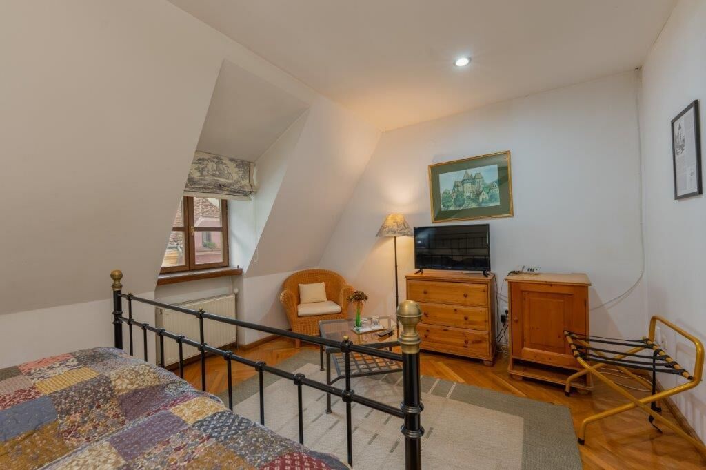A bedroom with a sloped ceiling, a bed, a chair, a dresser, a lamp, and a television.