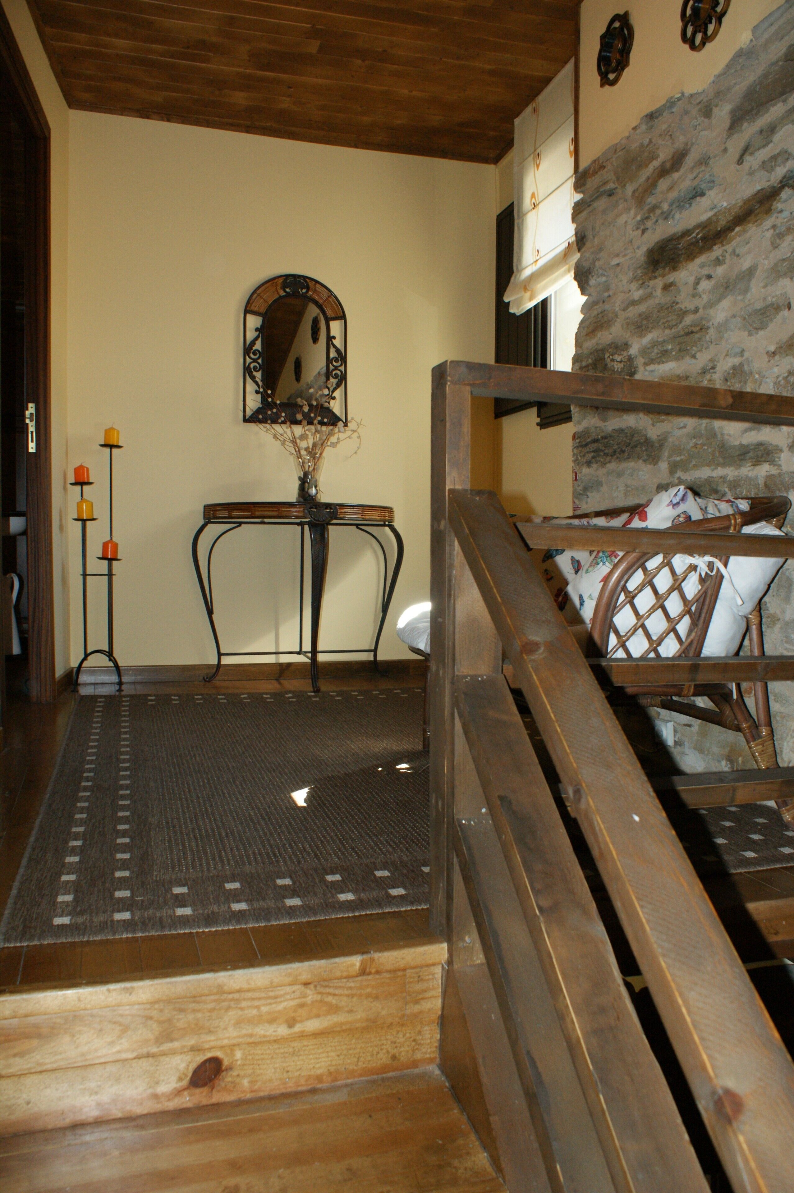 A wooden staircase leading to a room with a stone wall, a mirror, and a table with a vase.