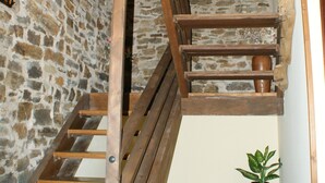 Un escalier en bois, avec des murs en pierre et une plante en pot.