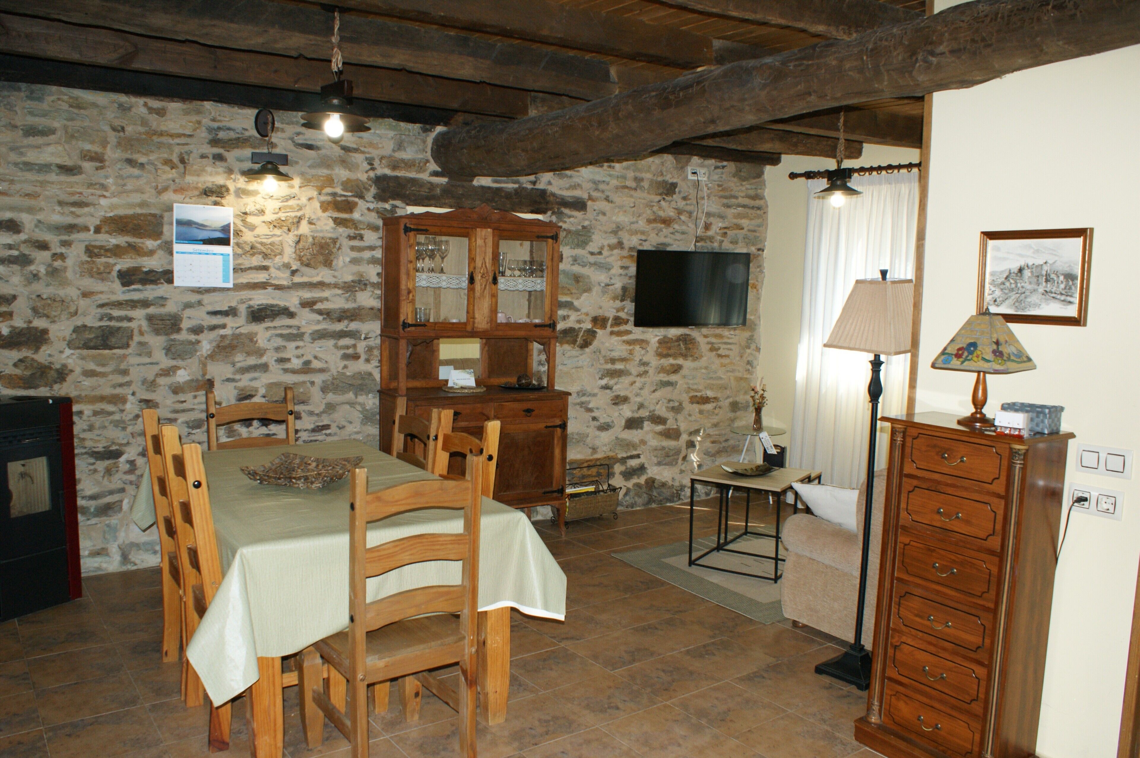 Quarto rústico com parede de pedra, móveis de madeira, mesa de jantar, televisão e abajur.