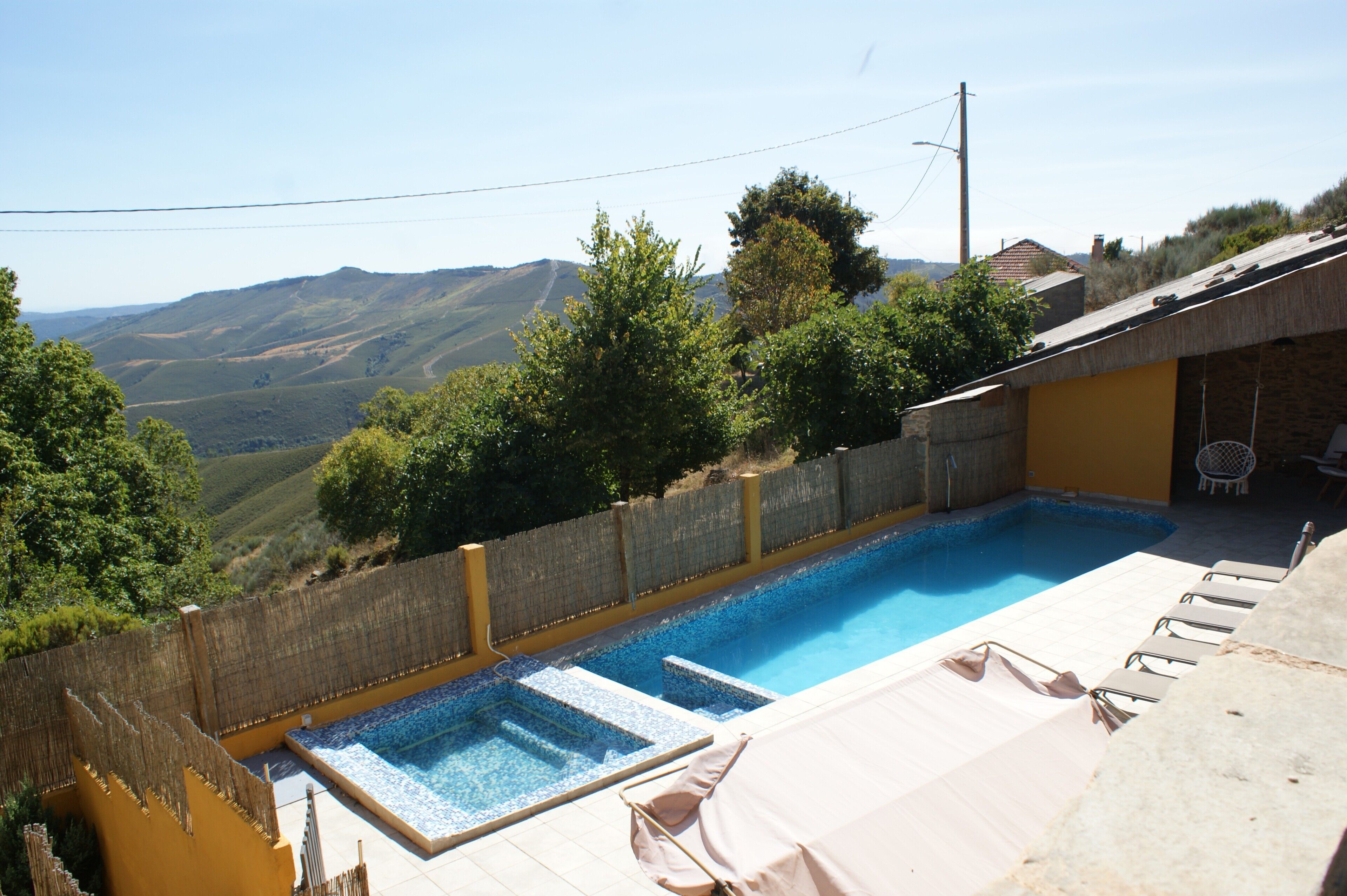 Piscina con vistas a colinas, zona de estar cubierta y un perímetro cercado.