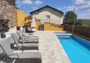 A swimming pool with lounge chairs, a small house, and a stone wall.