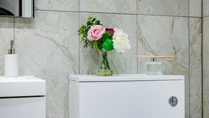 Um banheiro com pia branca, vaso sanitário e armário com um vaso de flores.