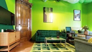 Une pièce avec un mur vert, un meuble en bois, un canapé vert, une table basse et un fauteuil gris.
