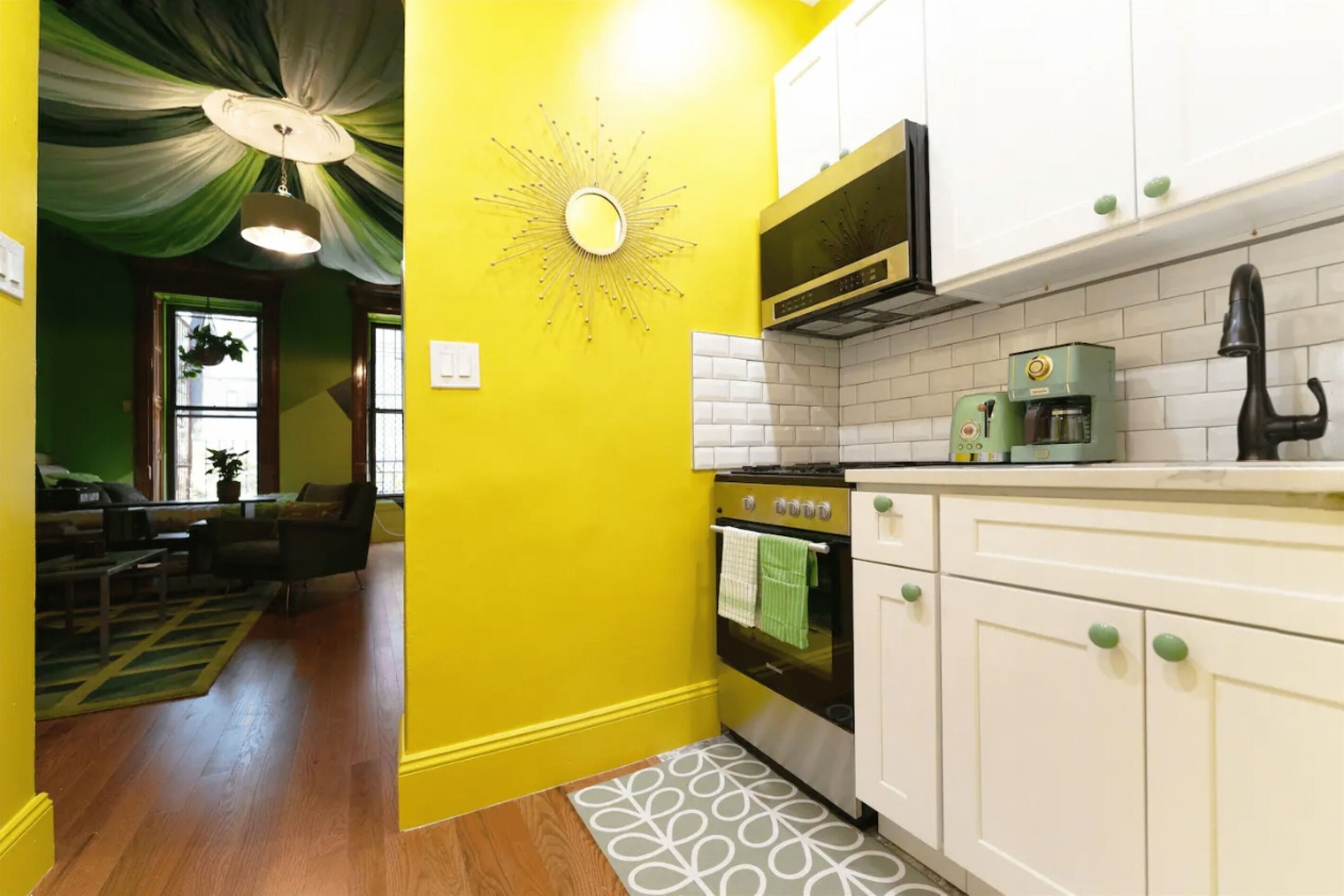 Una cocina con armarios blancos, un electrodoméstico verde y un adorno de pared con diseño de sol.