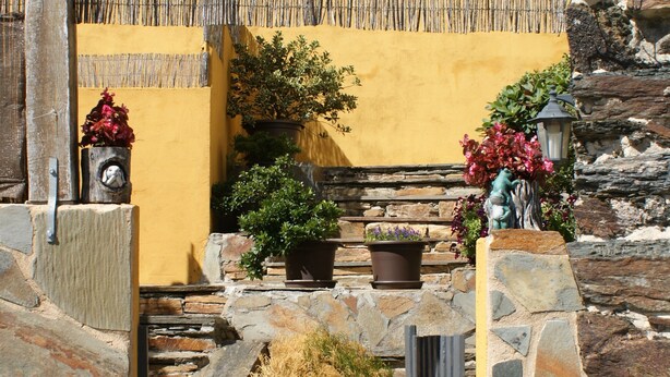 A stone archway leading to a yellow building with potted plants and a wooden fence.