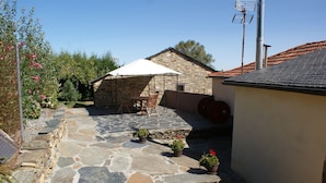 A stone patio with a table and chairs, a stone wall, and a building with a tiled roof.