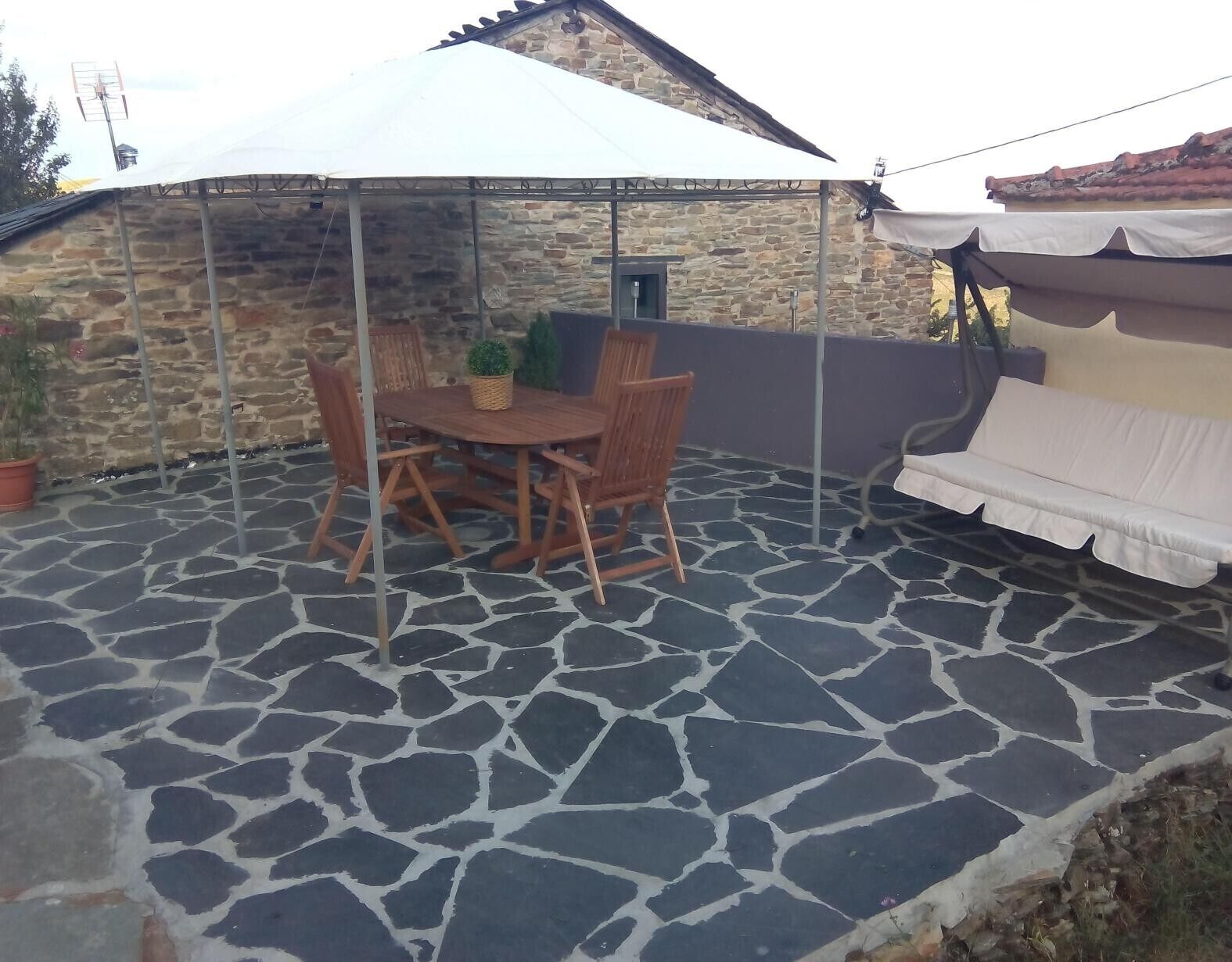 A stone patio with a table and chairs, a covered area, and a stone wall.