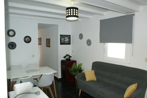 Un espace de vie comprenant un canapé, une table à manger avec des chaises, une plante en pot et des éléments décoratifs sur les murs.