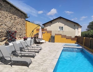Une piscine avec des chaises longues, un mur en pierre et un bâtiment jaune doté d’une fenêtre.
