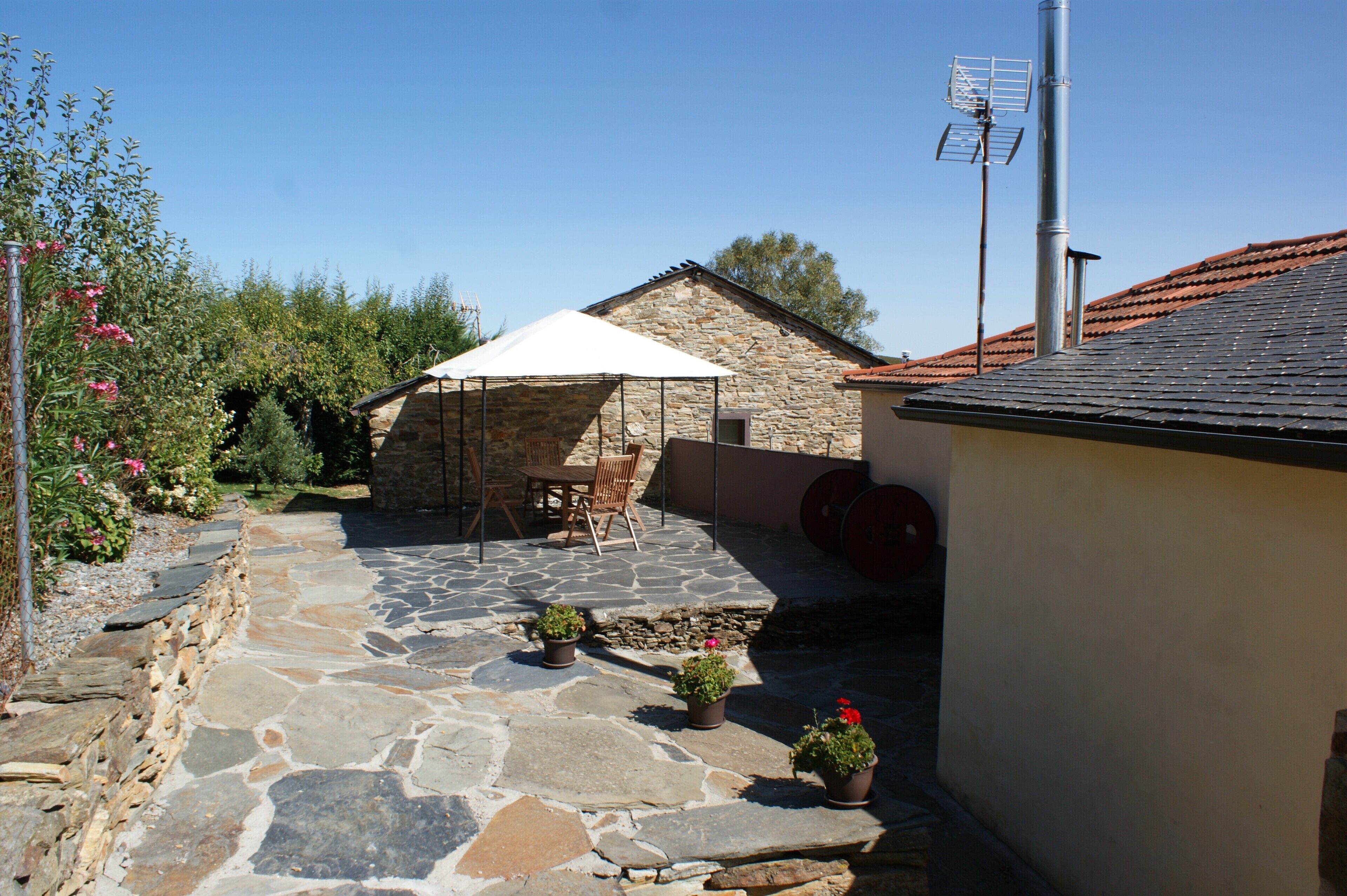 A stone patio with a table and chairs, a stone building, and potted plants.