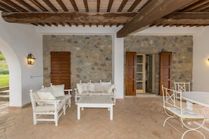 A covered patio with stone walls, a wooden ceiling, white furniture, and a stone fireplace. - Villa 'Cava Alta' with Sea View, Wi-Fi and Air Conditioning (Riparbella)