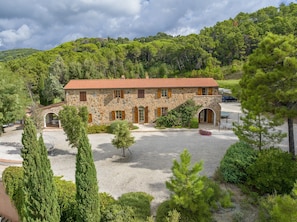 A stone building with a red-tiled roof, surrounded by a gravel courtyard and lush greenery. - Villa 'Cava Alta' with Sea View, Wi-Fi and Air Conditioning (Riparbella)