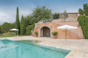 A swimming pool with a stone pathway, a covered seating area, and a stone building with a balcony. - Villa 'Cava Alta' with Sea View, Wi-Fi and Air Conditioning (Riparbella)