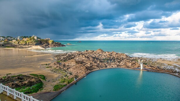 A coastal landscape with a rocky shoreline, a calm sea, and a white fence.
