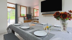A dining area with a table set for four, a flat-screen TV mounted on the wall, and a vase with flowers on the table.