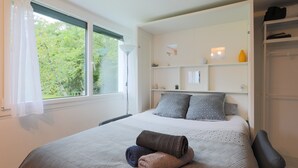 A bedroom with a bed, a window with curtains, a bedside table, and a wardrobe.