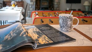 A magazine on a table with a patterned mug, a foosball table, and a fireplace in the background.