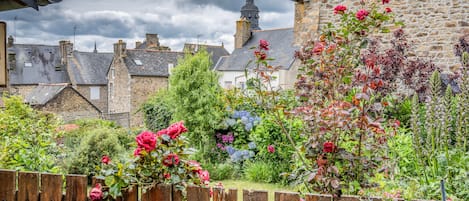 A garden with a wooden fence, stone buildings, and a variety of plants and flowers.