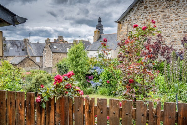 Un jardín con valla de madera, edificios de piedra y diversas plantas y flores.