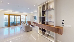 A modern living room with a sofa, a coffee table, and a built-in bookshelf. - King David Residences: Spacious 3-bdrs 3-bths with Pool, Gym & View in Jerusalem (Jerusalem)