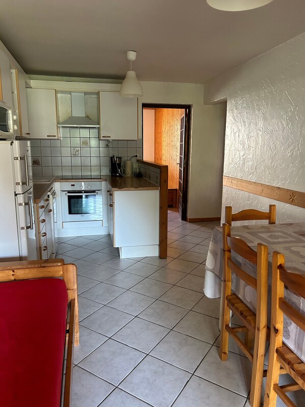 A compact kitchen with white cabinets, a microwave, an oven, and a wooden dining table with chairs.
