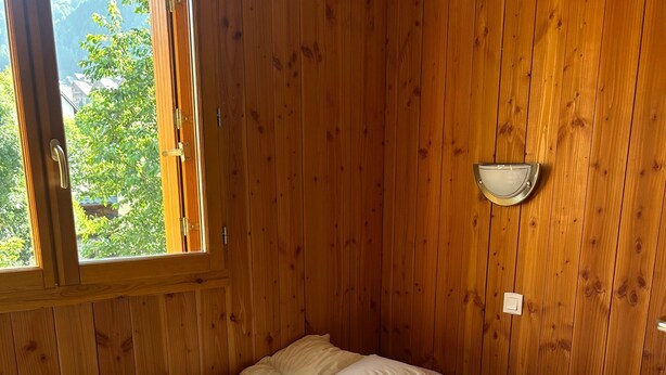 A wooden room with a bed, a window, and a wall-mounted light fixture. - Apartment 'La Sétaz' with Mountain View, Private Terrace and Wi-Fi (Valloire)