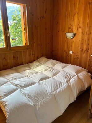 Una habitación de madera con una cama, una ventana y una lámpara fijada a la pared.