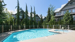 A swimming pool with a surrounding deck, a chair, and tall trees.