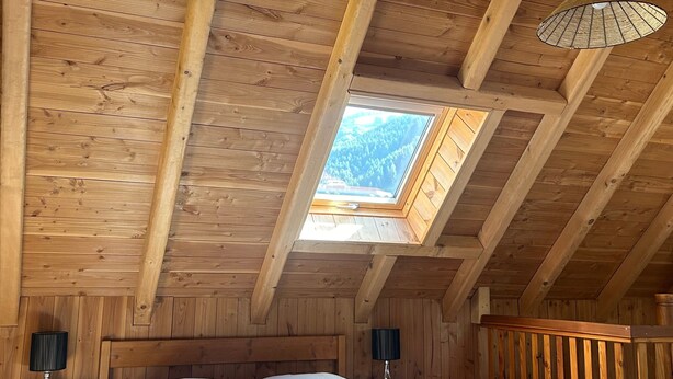 A wooden cabin bedroom with a skylight, a bed, and a hanging light fixture.