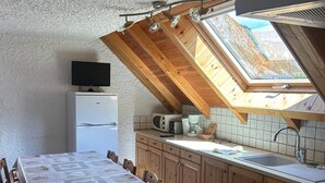 A compact kitchen with a dining area, wooden cabinets, a built-in microwave, and a television on a white cabinet.